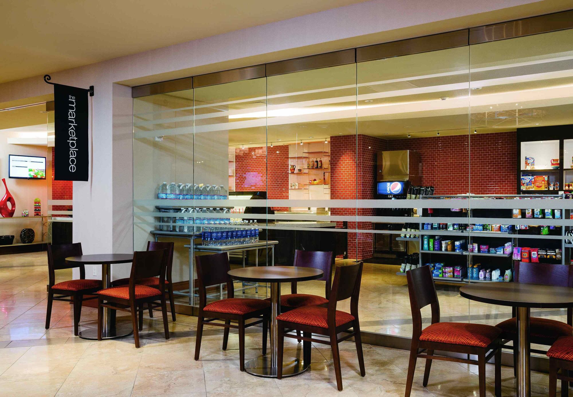A modern restaurant with glass partitions, red-brick walls, and a variety of seating options including round tables and chairs.
