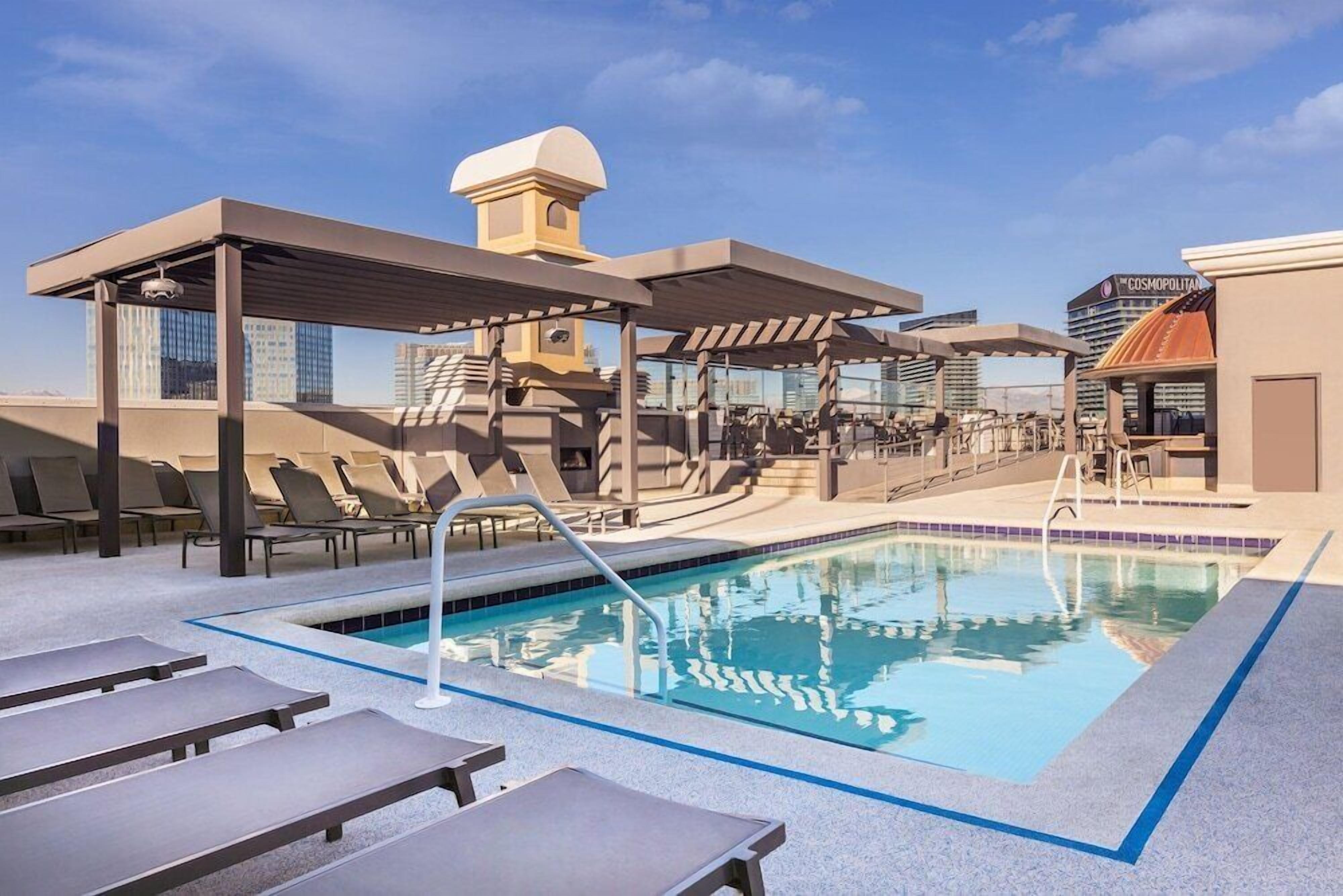A rooftop pool area with lounge chairs and a covered seating area.