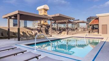 A rooftop pool area with lounge chairs and a covered seating area.