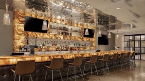 Zona de bar moderna con una barra alargada, varios taburetes y una pared decorativa con una pantalla de televisión.