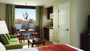 A hotel room with a bed, green armchair, dining table, and a view of the cityscape.