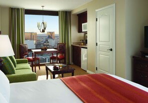 A hotel room with a bed, green armchair, dining table, and a view of the cityscape.