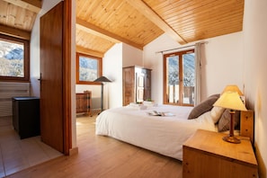 A bedroom with a large bed, wooden ceiling, and windows overlooking a snowy landscape.