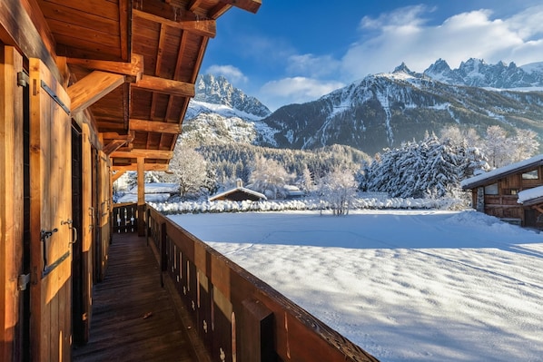 A wooden cabin with a balcony overlooking a snowy landscape and mountains.