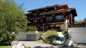 Un edificio de madera de varios pisos con balcones, un garaje y un camino de entrada con rocas grandes.