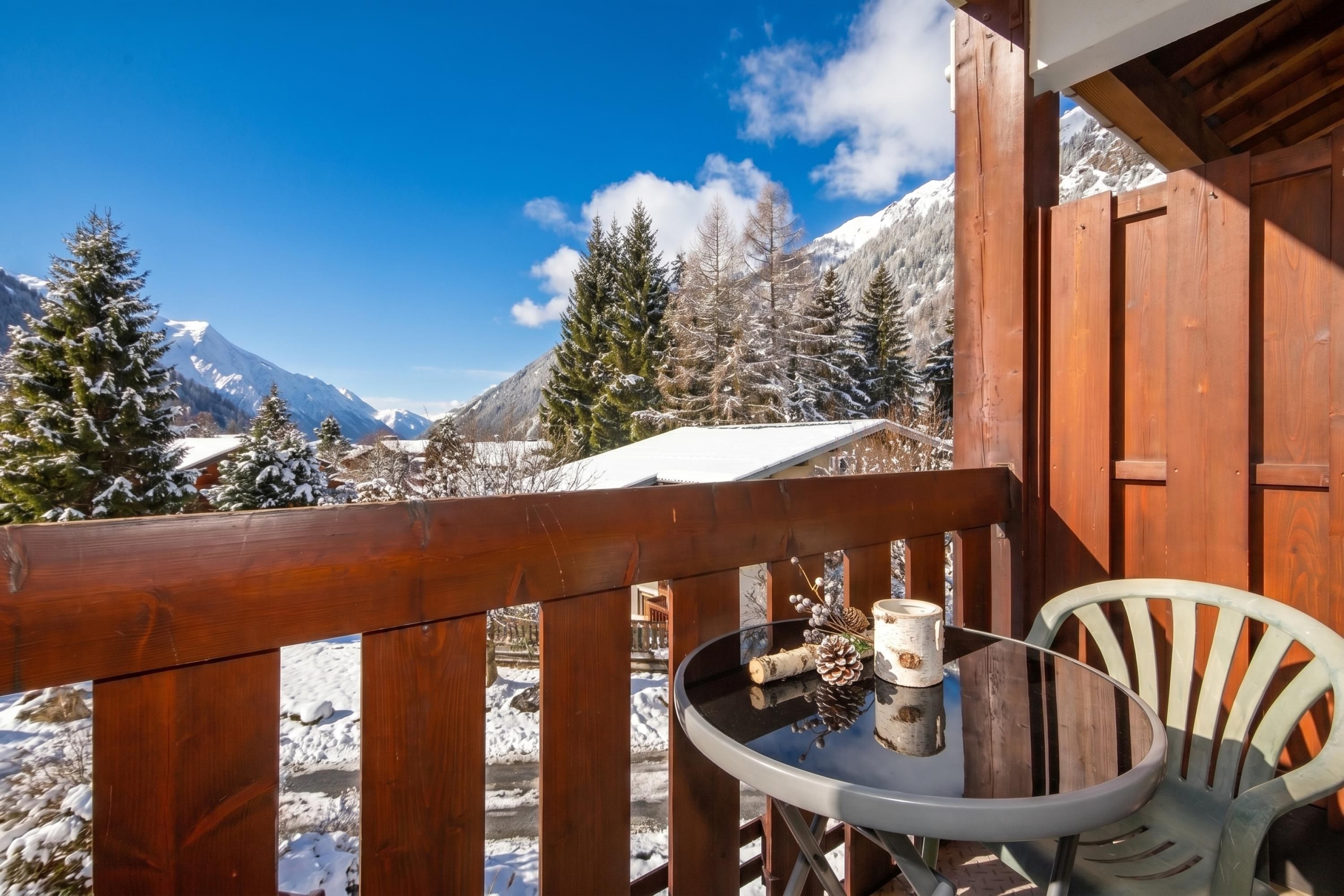 A wooden deck with a table and chairs, overlooking a snowy mountain landscape.