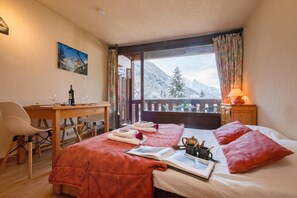 Ein Hotelzimmer mit Bett, Schreibtisch, Stuhl, Fenster mit Bergblick und einem Bild an der Wand.
