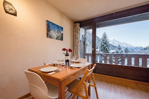 Ein Essbereich mit einem Holztisch, gedeckt für zwei Personen, einem Gemälde an der Wand und Blick auf schneebedeckte Berge durch ein großes Fenster.