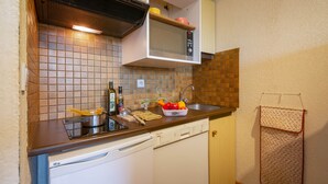 Cocina compacta con microondas, lavamanos y lavavajillas. Hay varios utensilios de cocina en la encimera, incluyendo una tabla de cortar, un cuenco de fruta y una botella de aceite de oliva.