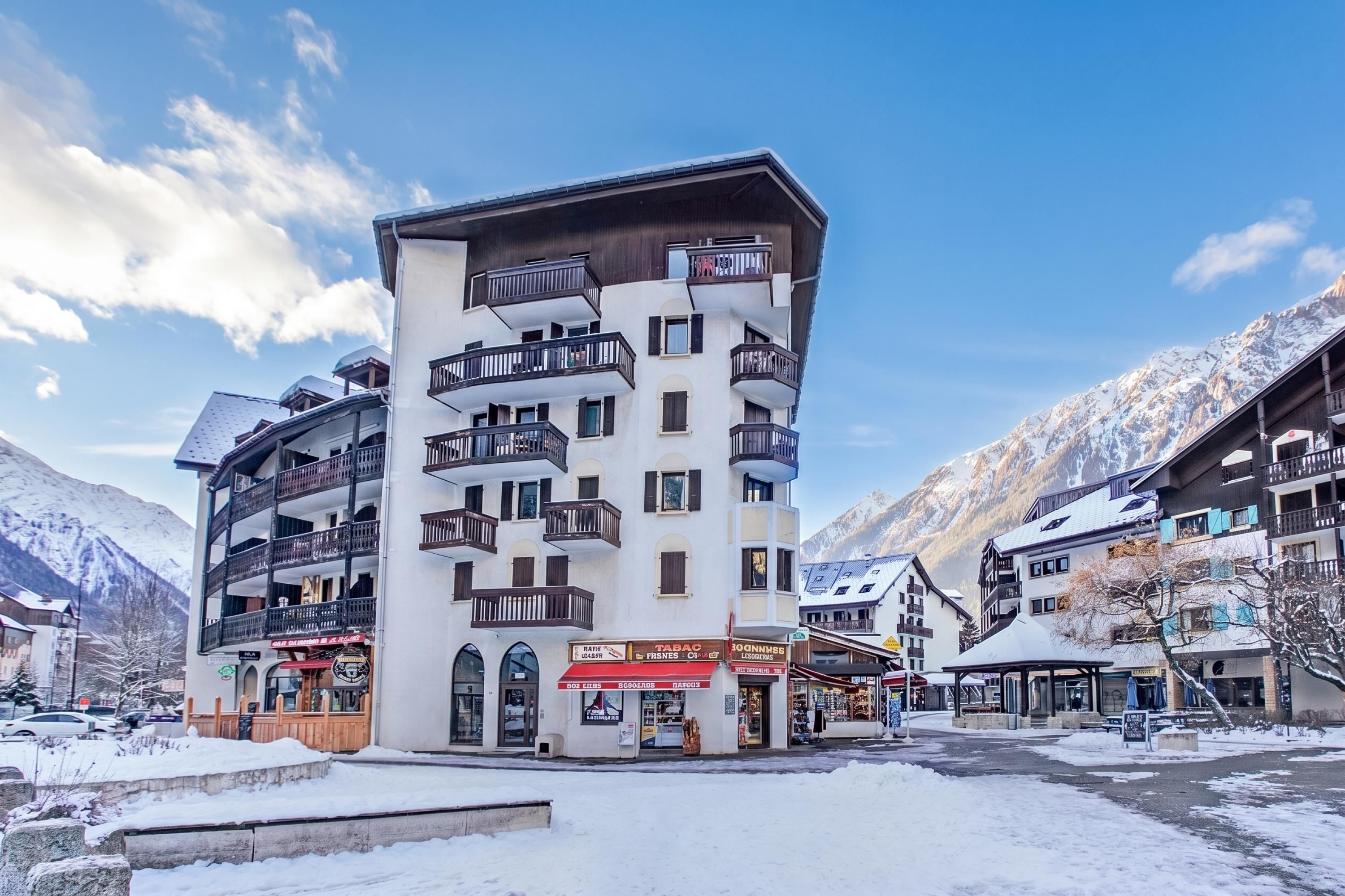 Un hôtel à plusieurs étages doté de balcons, une station de ski en arrière-plan et un paysage enneigé.