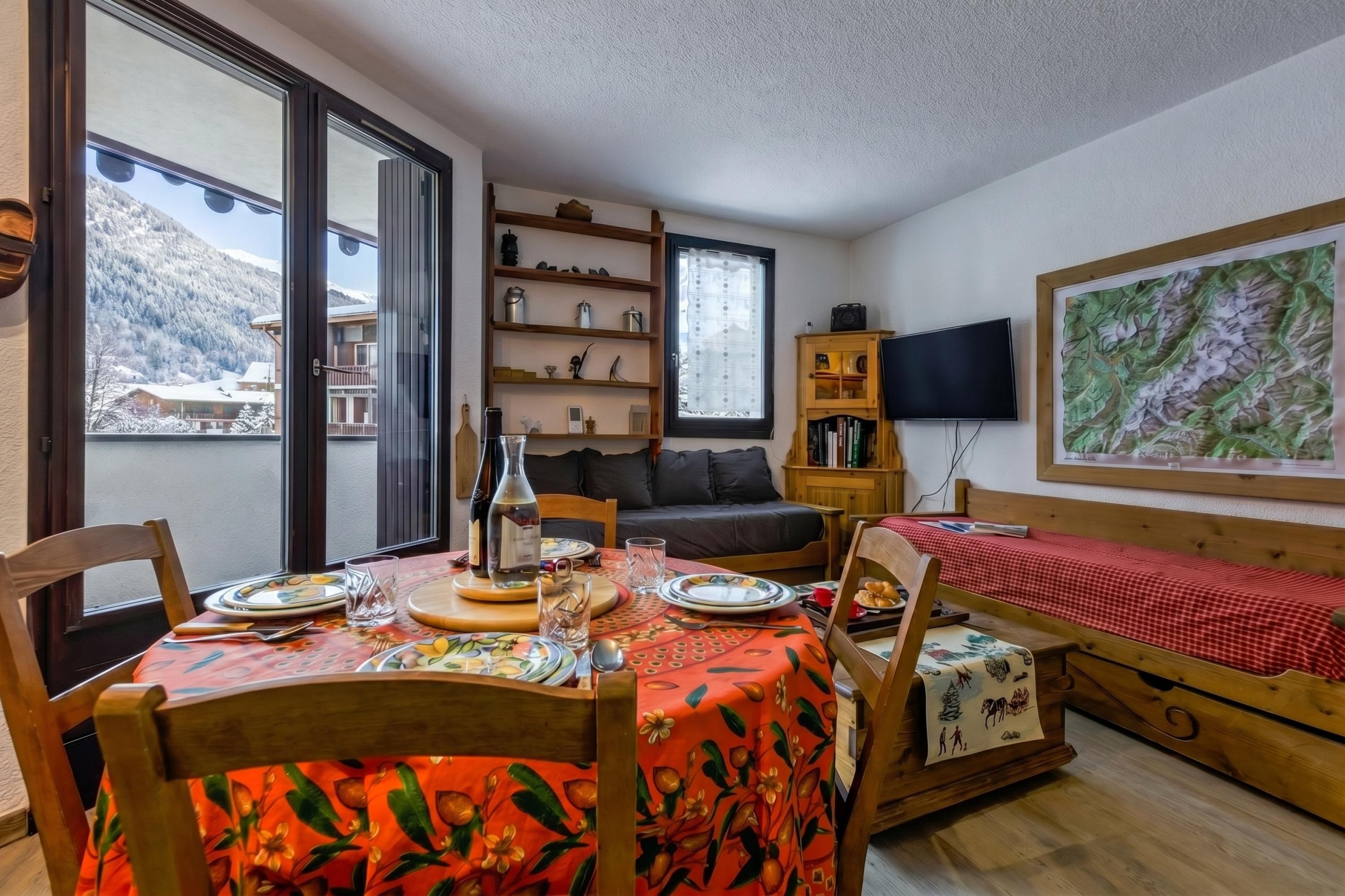 A cozy room with a dining table set for two, a sofa, a TV, and a bookshelf.