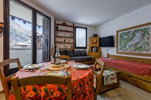 A cozy room with a dining table set for two, a sofa, a TV, and a bookshelf.