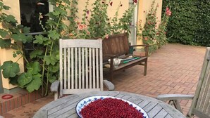 Une terrasse avec une table ronde, un banc en bois et un saladier rempli de baies rouges.