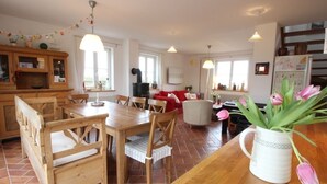 Un salon chaleureux avec une table à manger en bois, des chaises, un canapé rouge et une table basse blanche. On peut voir un vase blanc rempli de tulipes sur la table.