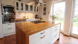 Une cuisine moderne avec des meubles blancs, un plan de travail en bois, un four encastré et une fenêtre donnant sur l’extérieur.