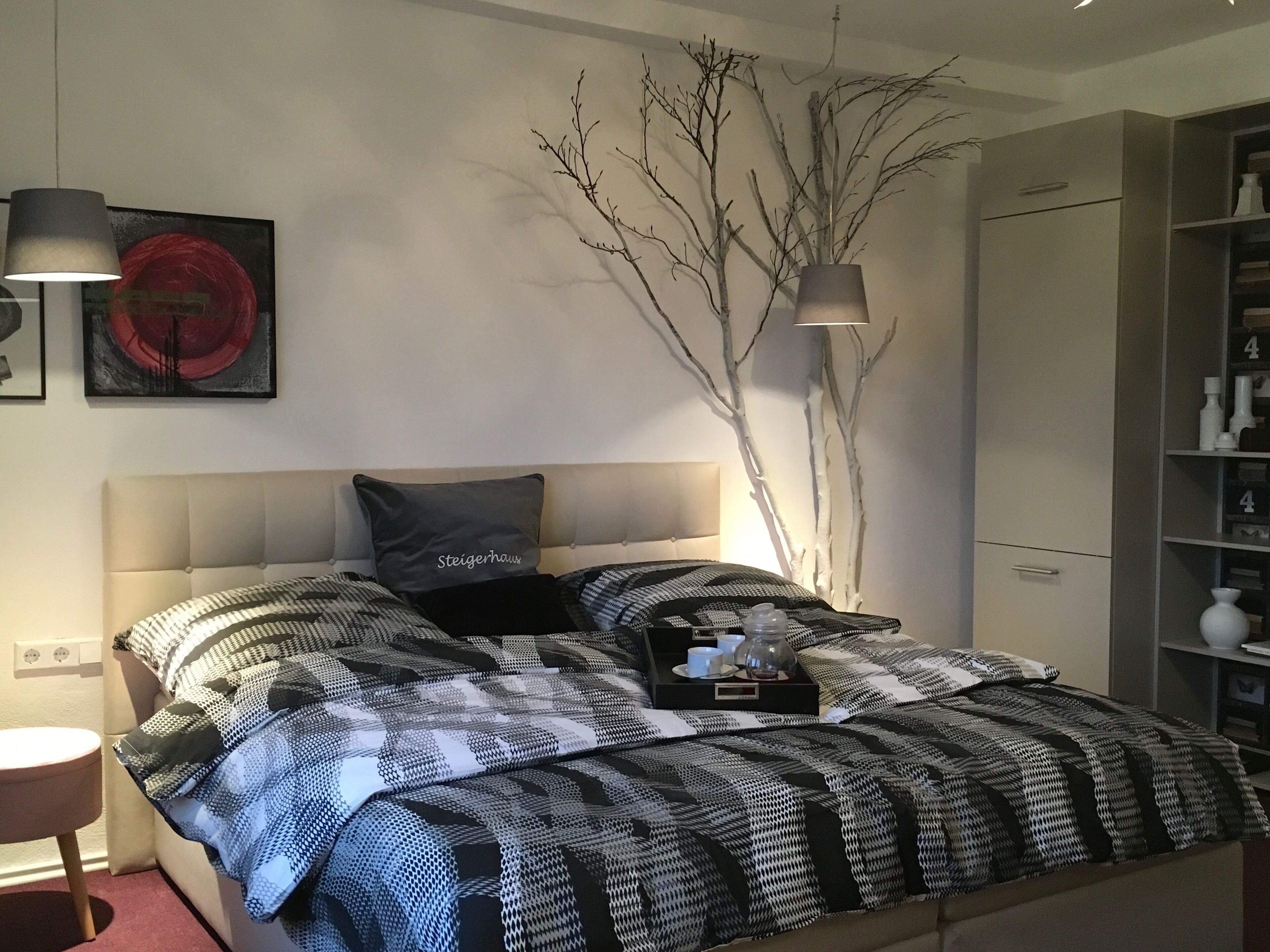 Une chambre à coucher moderne avec une tête de lit capitonnée, une couvre-lit à motifs, une table de chevet et une petite table de nuit.