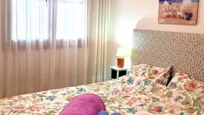 Uma cama com roupa de cama floral, cabeceira com design estampado e um quadro de uma praia na parede.