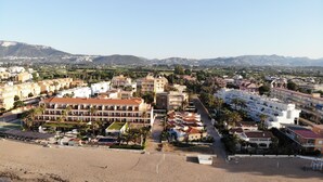 Um resort costeiro com vários edifícios, uma praia e montanhas ao fundo.