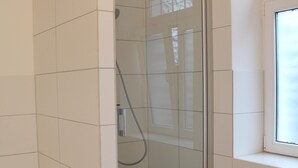 Una doccia con porta in vetro, un tavolino e una finestra in un bagno con piastrelle bianche.