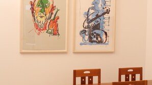 Un'area pranzo con tavolo e sedie in legno, due quadri appesi al muro e pavimento in legno.