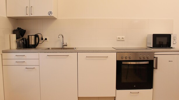 Una cucina moderna con mobili bianchi, lavello in acciaio inossidabile, macchina da caffè, forno a microonde e forno integrato.