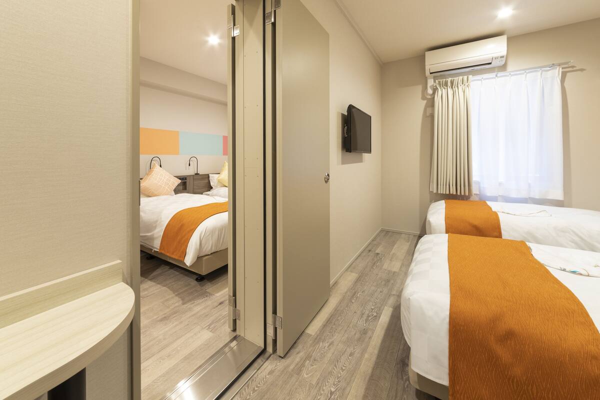 A hotel room with two beds, a sliding door, a flat-screen TV, and an air conditioning unit.