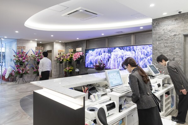 A reception area with a marble counter, a large flat-screen TV, and a modern interior design. - SARASA HOTEL Dotonbori (Osaka)