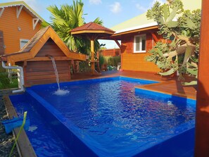 Piscina com deck de madeira, rodeada por edifícios de madeira e cactos.
