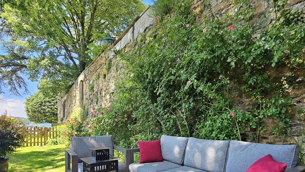 An outdoor seating area with a sofa and table, surrounded by greenery and a stone wall. - La Bâtie, La Tour: duplex apartment. (Vienne)