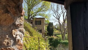 A stone building with a garden view, including a metal railing and a variety of plants. - La Bâtie, La Tour: duplex apartment. (Vienne)