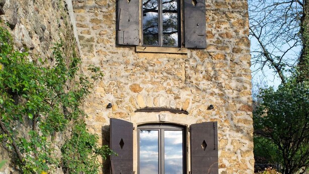 A stone building with a rustic exterior, a wooden door, and a small outdoor seating area with a table and chairs. - La Bâtie, La Tour: duplex apartment. (Vienne)