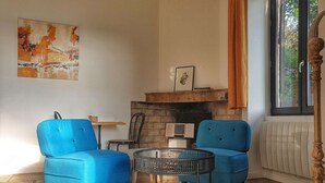 A living room with two blue armchairs, a small round table, a fireplace, and a window with curtains. - La Bâtie, La Tour: duplex apartment. (Vienne)