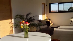 Un comedor moderno con una mesa redonda blanca, sillas de madera y un florero con flores.