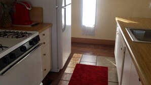 A kitchen with a white refrigerator, a red coffee maker, a gas stove, and a red rug.