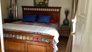 A bedroom with a wooden bed, colorful bedding, a nightstand with a vase, and a painting on the wall.