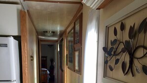 A narrow hallway with wooden flooring, a white refrigerator on the left, and a wall-mounted decorative piece on the right.