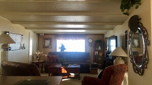 A living room with a sofa, armchairs, a coffee table, and a TV. There is a window with a view of a person outside.