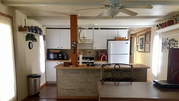 A kitchen with a central island, white cabinets, a refrigerator, and a ceiling fan.