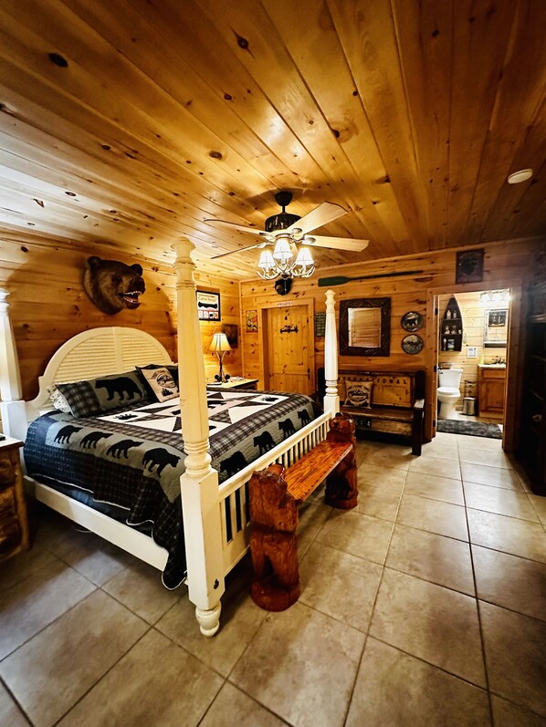 A four-poster bed with a bear head mounted above it, a chandelier, and a wooden bench with a bear carving.