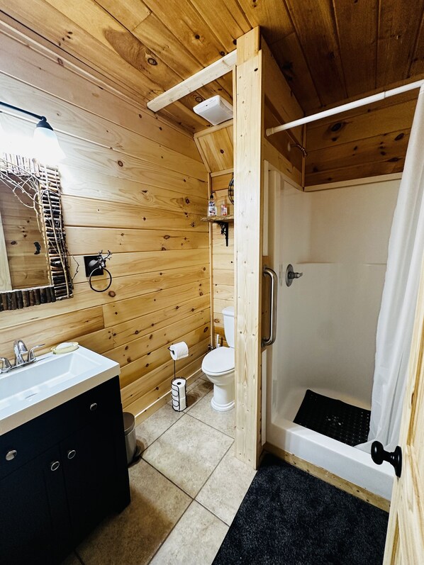 Une salle de bain aux murs lambrissés, équipée d’un lavabo, de toilettes et d’une douche.