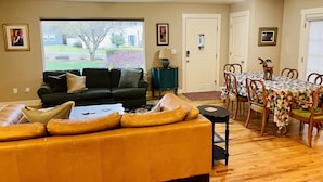 A living room with a yellow sofa, a dark green couch, and a dining table with chairs. There are two doors, a window, and a lamp on a side table. - Great location for visiting the NW. Comfortable 5 bedroom home. (Portland)