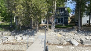 Un muelle de madera que lleva a una casa con un sendero de piedra y árboles.