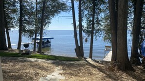 Un patio junto al lago con un camino de piedra que lleva a un muelle, rodeado de árboles altos y una vista despejada del agua.