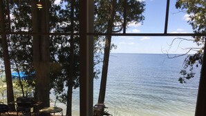 Vista de un lago desde una ventana con un patio de piedra y mobiliario exterior.