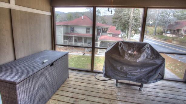 Un barbecue abrité sur une terrasse en bois, offrant une vue sur les maisons à travers de grandes fenêtres.