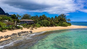 A beachfront property with a house, clear turquoise waters, and a mountainous backdrop. - Haena Beachfront With Stunning Panoramic Ocean Views TVNC # 5134  (Hanalei, Haena)