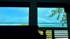 A room with a view of the ocean and a rainbow through a window. - Haena Beachfront With Stunning Panoramic Ocean Views TVNC # 5134  (Hanalei, Haena)