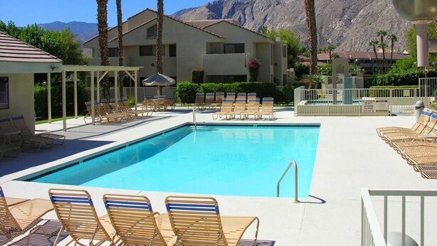 A pool area with lounge chairs, a building with a flat roof, palm trees, and mountains in the background. -  DOWNTOWN PALM SPRINGS POOLSIDE LOWER  CONDO STEPS TO CASINO   (Palm Springs)