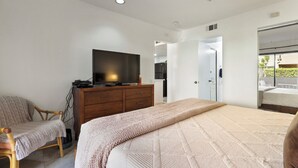 A bedroom with a bed, a TV on a dresser, a chair, and a view of the outside balcony. -  DOWNTOWN PALM SPRINGS POOLSIDE LOWER  CONDO STEPS TO CASINO   (Palm Springs)