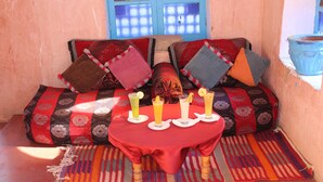 A cozy seating area with a red table, colorful cushions, and a window with blue shutters. - Dar Timitar Eco lodge  (Kelâat M'Gouna)